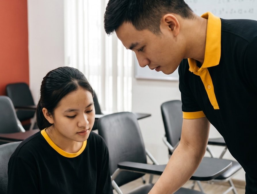 Giáo viên GTL cúi xuống chỉ bài cho một học viên đang ngồi đọc sách