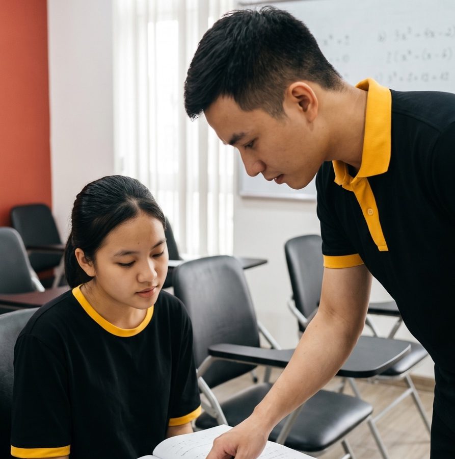 Giáo viên GTL cúi xuống chỉ bài cho một học viên đang ngồi đọc sách